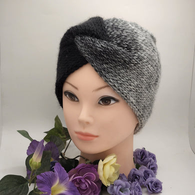 Messy bun ear warmer in colors flowing from black to grey displayed on a manikin surrounded by purple flowers