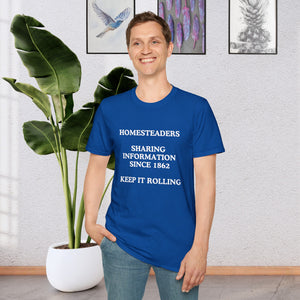 a man standing in a room in front of a plant wearing a Royal Blue T-shirt that says Homesteaders sharing information since 1862 Keep it rolling