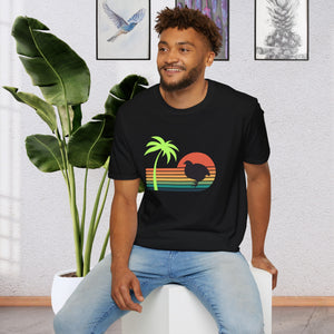 A man wearing a black T-shirt that has a color line sunset ranging from orange at the top to teal at the bottom. There is a coturnix quail in the middle of the sun and there is a vibrant green palm tree .