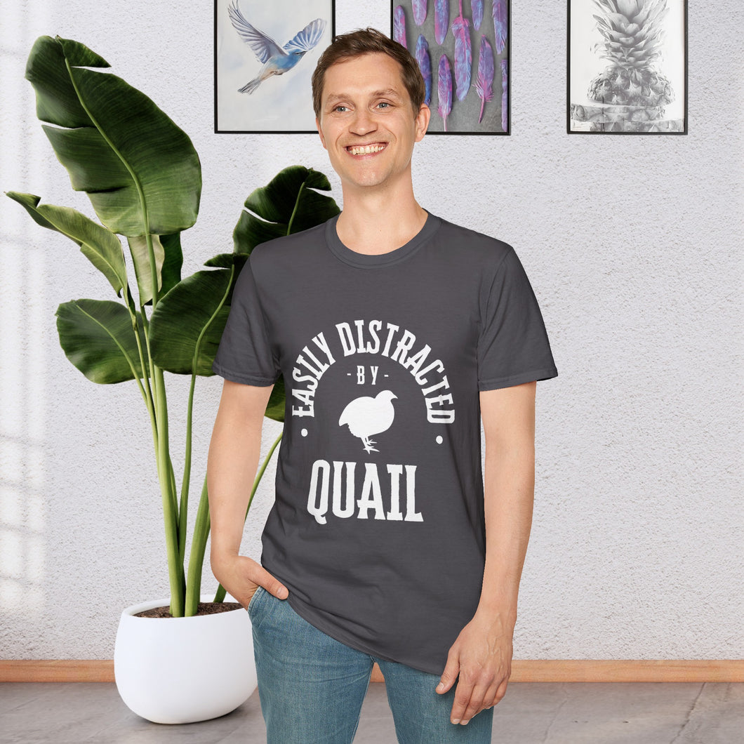 A man standing in front of a plant wearing a Charcoal Grey T-shirt that says Easily distracted by Quail in white lettering. The shirt has a silhouette of a quail in the center.