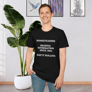 a man standing in a room in front of a plant wearing a black T-shirt that says Homesteaders sharing information since 1862 Keep it rolling