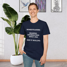 a man standing in a room in front of a plant wearing a Navy Blue T-shirt that says Homesteaders sharing information since 1862 Keep it rolling